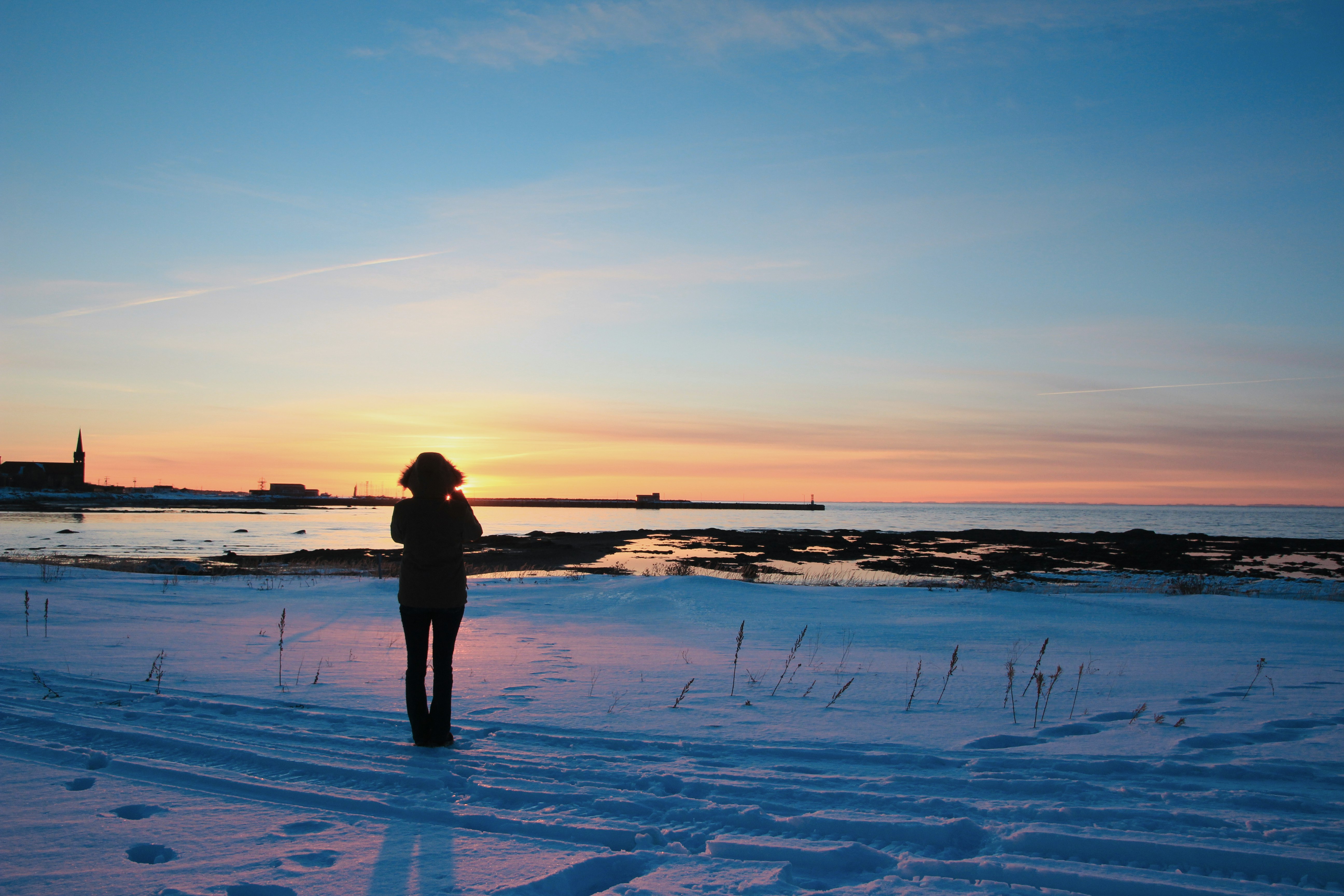 silhouette of person standing on snow covered ground during sunset